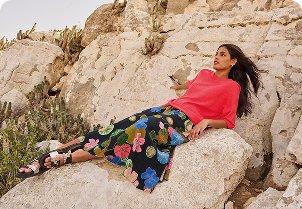 a woman in a dress sitting on a rock in the desert